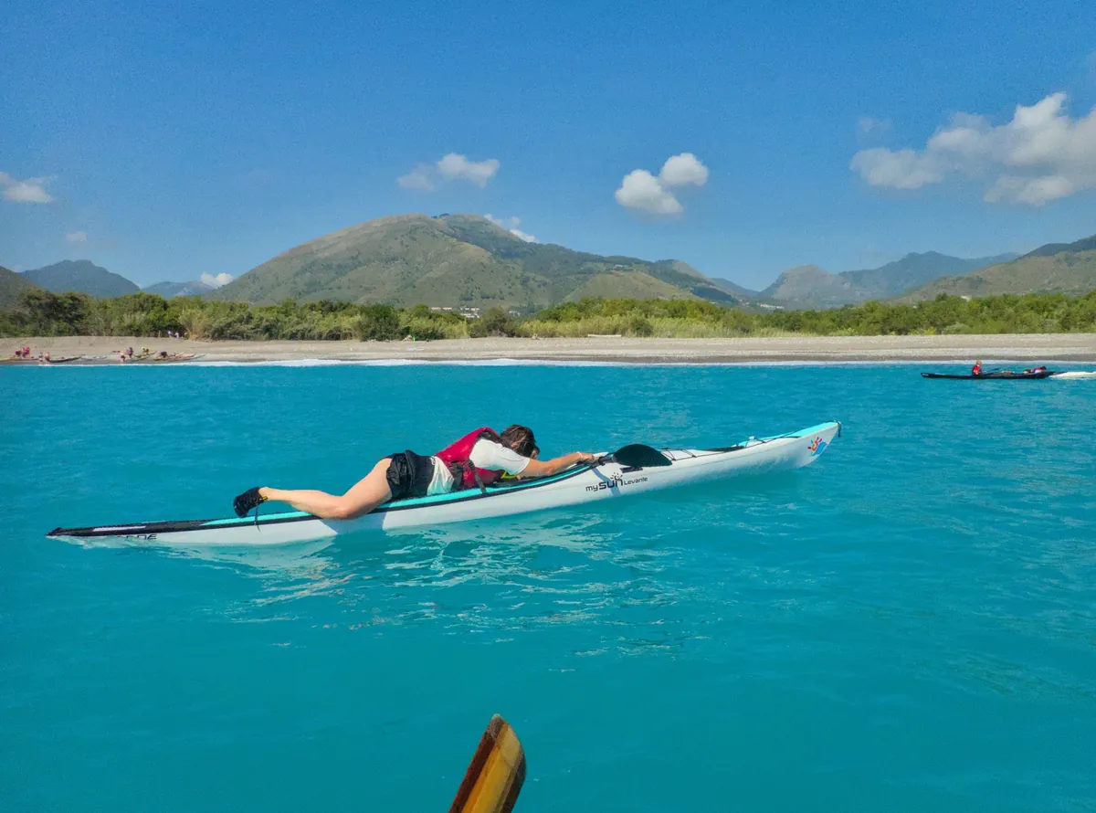 Che cosa certifica un livello Pagaia Azzurra: esercizio di rientro nel kayak da mare, con il corpo disteso sul ponte, in acqua turchese