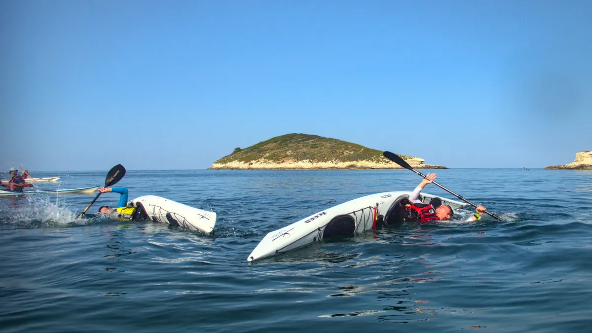 Autosoccorso nel kayak da mare: due pagaiatori rovesciati in acqua profonda durante un’esercitazione, con un isolotto sullo sfondo