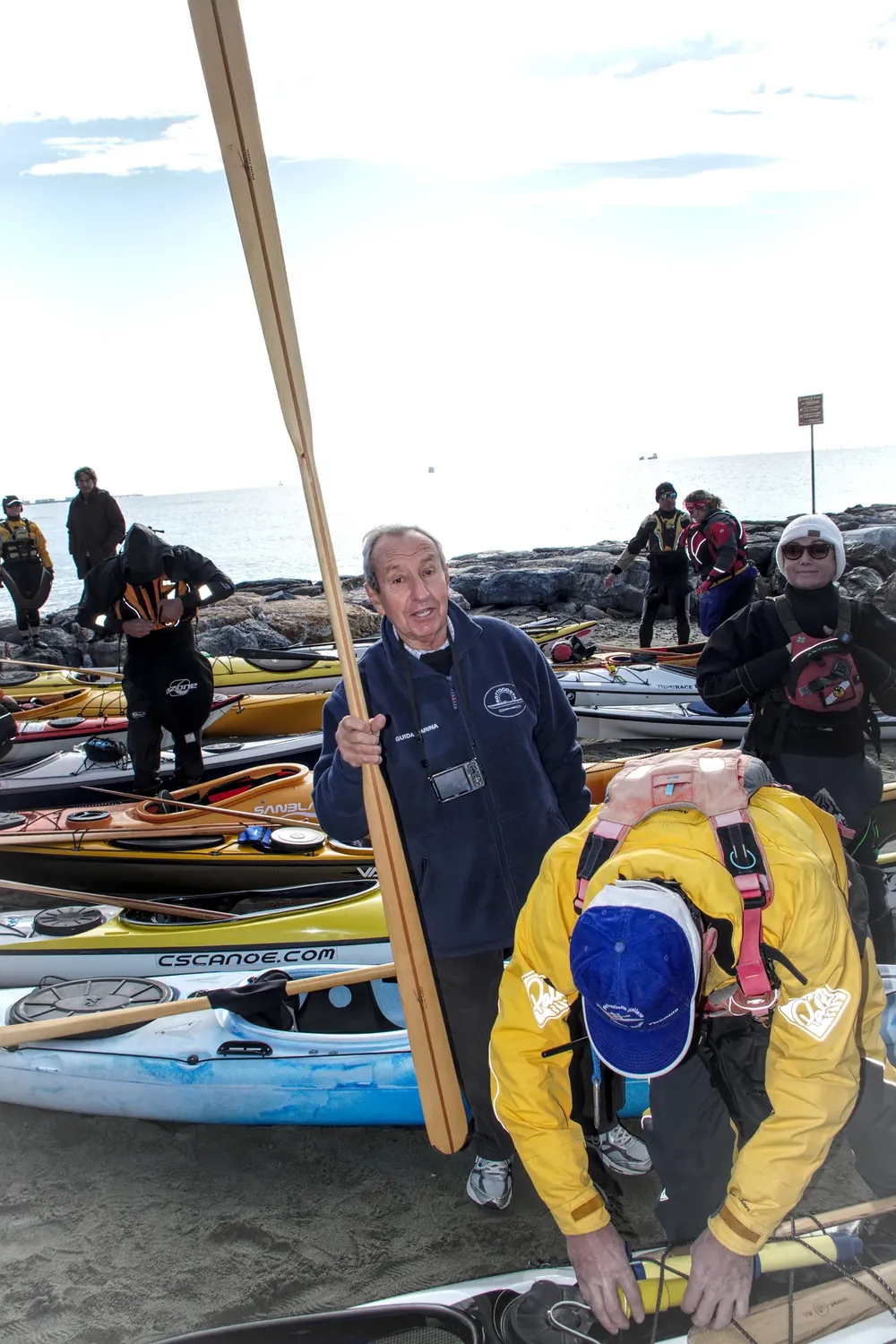 Dalla canoa eschimese al kayak groenlandese: pagaiatore con una pagaia groenlandese in legno, a pala stretta e lunga, fra i kayak sulla spiaggia