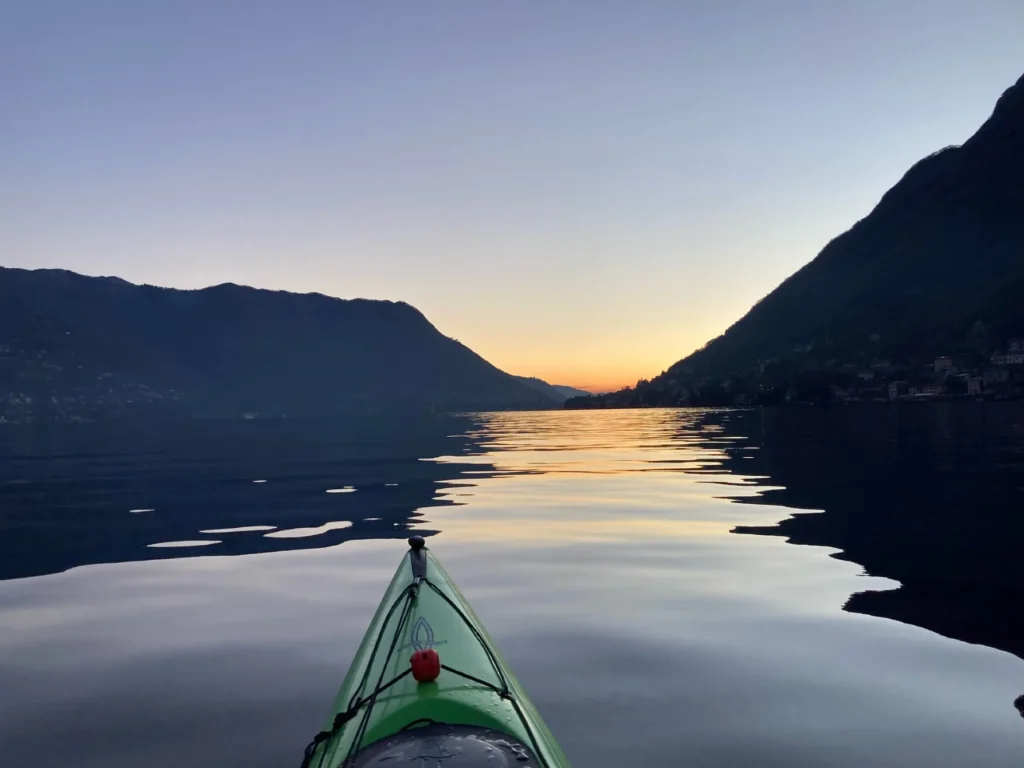Circumnavigazione Invernale in Kayak del Lago di Como: prua del kayak sul lago calmo all'alba tra le montagne