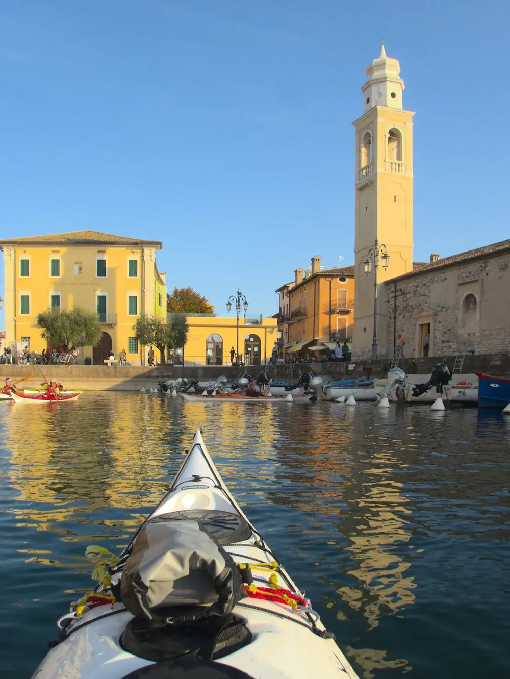 Scuole e club di kayak da mare: rientro in un piccolo porto, visto dalla prua del kayak, con il campanile sullo sfondo
