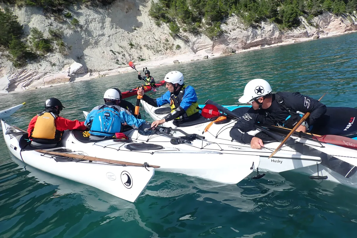 Corso di kayak da mare: un gruppo con caschi e aiuti al galleggiamento affiancato in acqua, sotto una falesia bianca