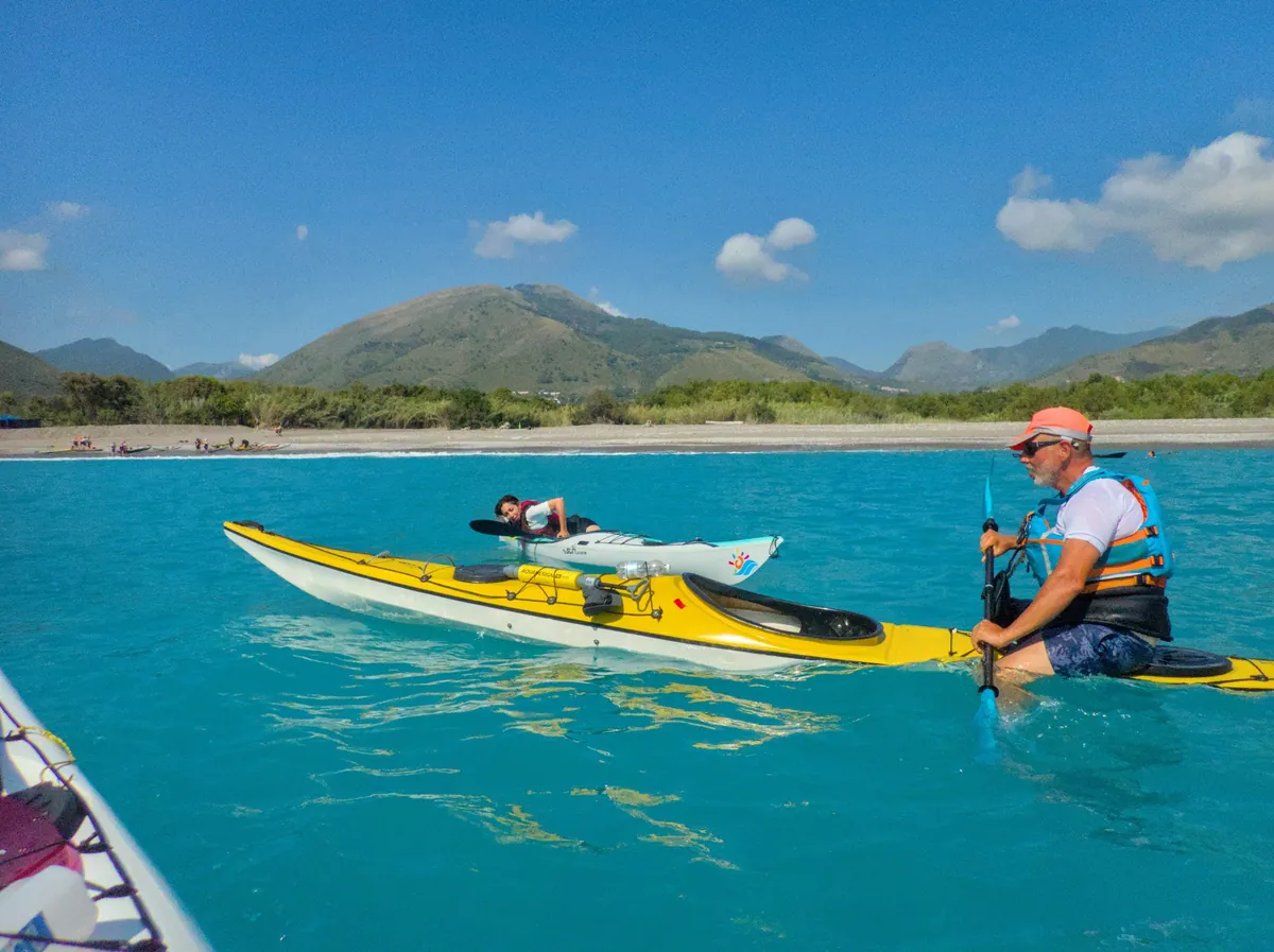 Diventare istruttore di kayak da mare: esercitazione in acqua, con un pagaiatore che tiene il kayak e un altro che risale sul suo