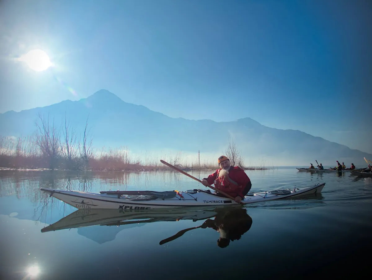 Trova un istruttore di kayak da mare: pagaiatore sul lago calmo, con le montagne sullo sfondo