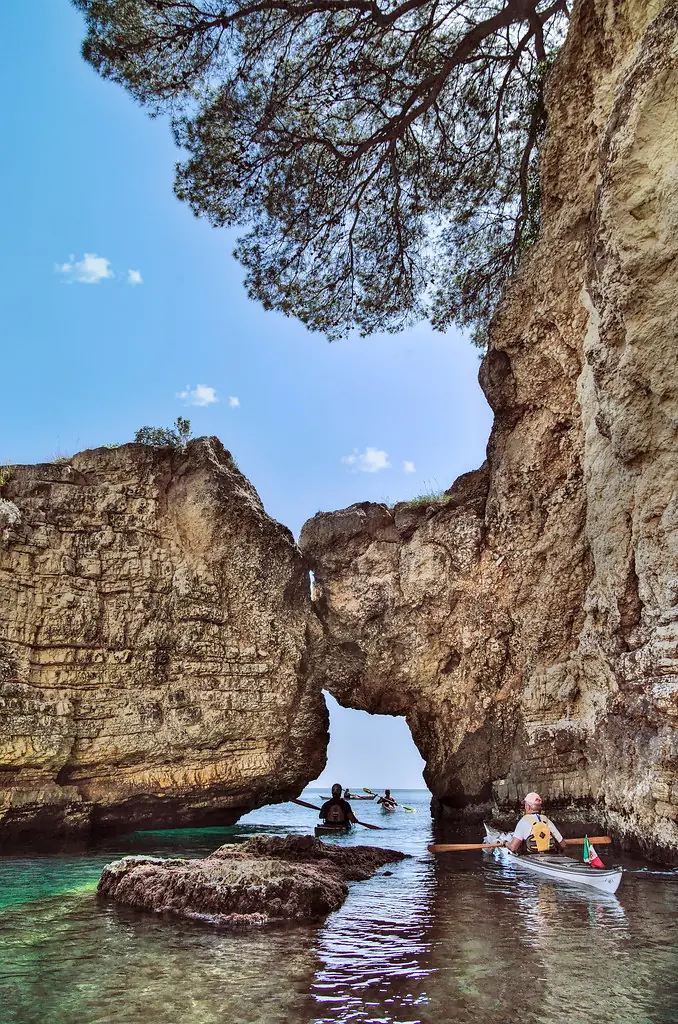 La storia di Sottocosta: kayak da mare sotto un arco di roccia, con un pino sulla falesia