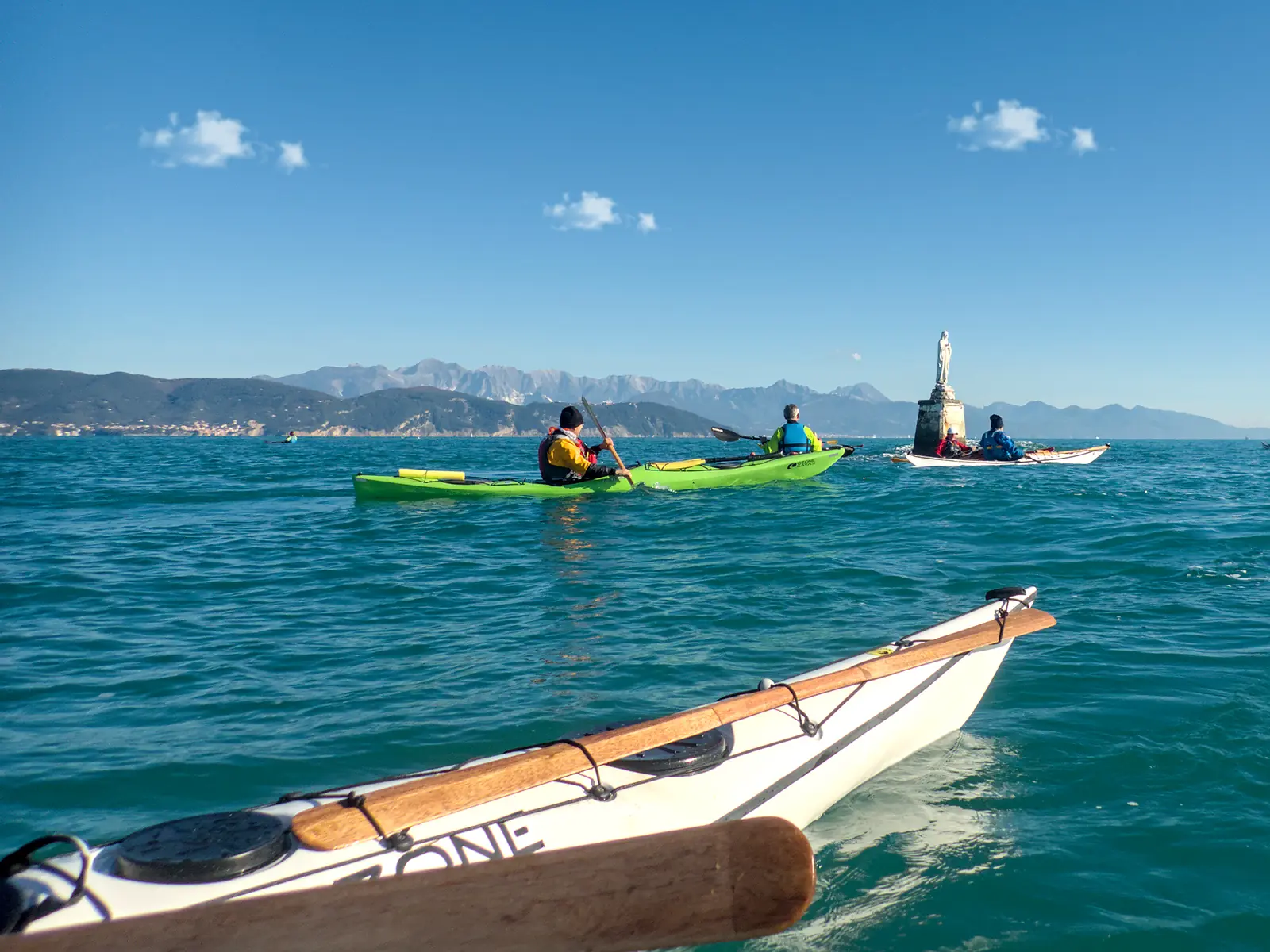 La storia di Sottocosta: kayak da mare in navigazione verso una statua in mare, con le montagne sullo sfondo