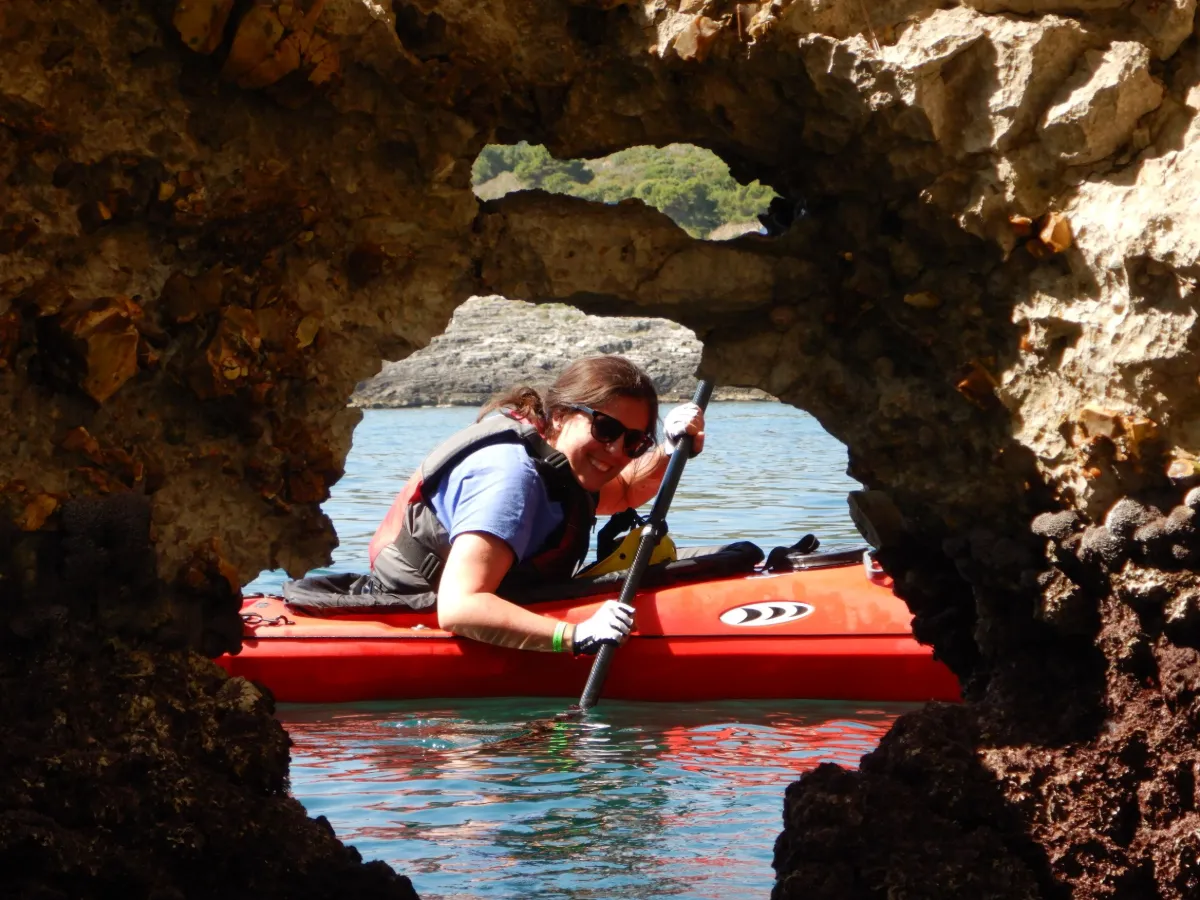 Conoscere la costa per l’esame Pagaia Azzurra: pagaiatrice in kayak da mare rosso dentro un arco di roccia, al Kayak Camp 2019 sul Gargano
