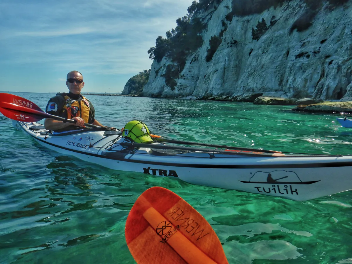 Tipi di kayak da mare: pagaiatore seduto in un kayak a ponte chiuso, con la pagaia a doppia pala in primo piano